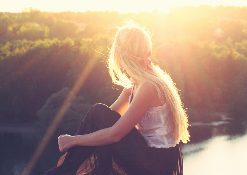 Woman facing the sun, with a view of a river and trees